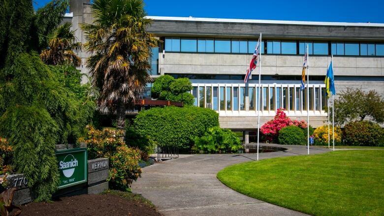 A municipal hall with flags outside is pictured on a sunny day. A sign reads 'Saanich inc. 1906' in the bottom left of the image.