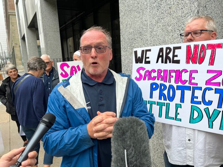 man stands outside near someone holding a white sign.