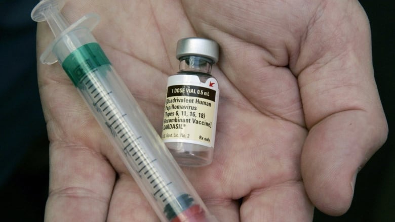 A hand holds a syringe and a vial of vaccine with a label that says human papillomavirus vaccine.