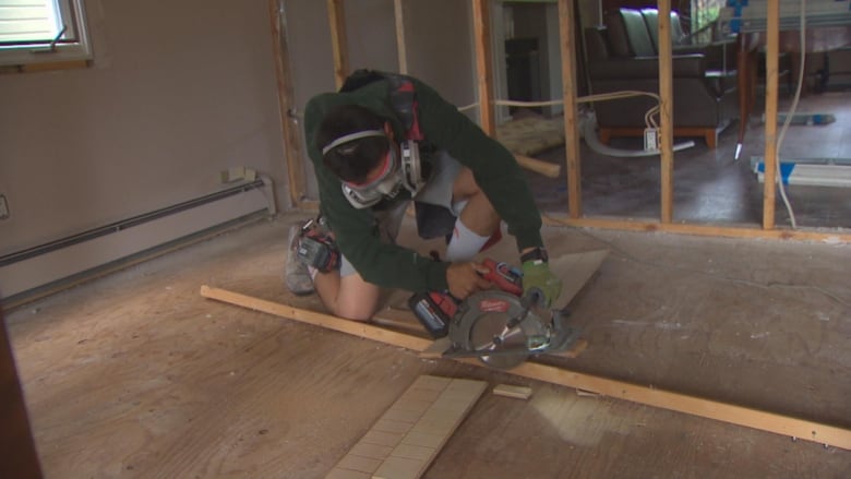 A man wearing a respirator cuts lumber with a circular saw in a home.