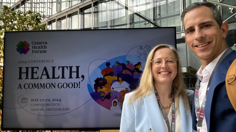 The doctors stand, smiling, in front of a sign for the Geneva Health Forum