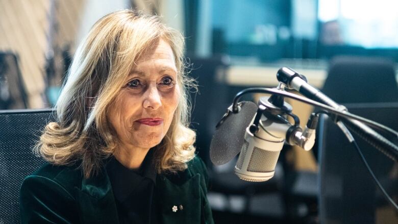 A woman sitting in a studio speaking into a mic. 