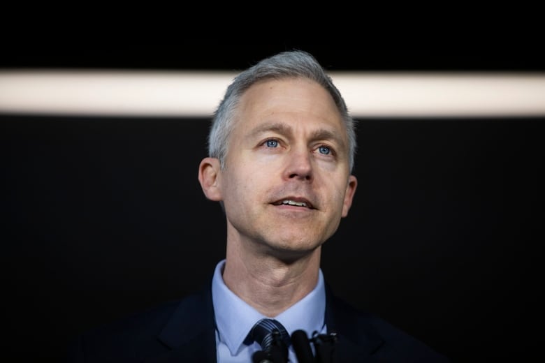 A white man with white hair looks up at a news conference.