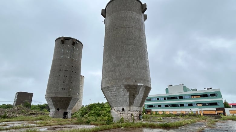 Three large cement cilos stand on an abandoned lot along with a green office building on a rainy day.