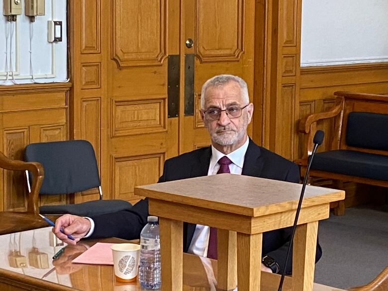 A man wearing a suit sits in a courtroom.