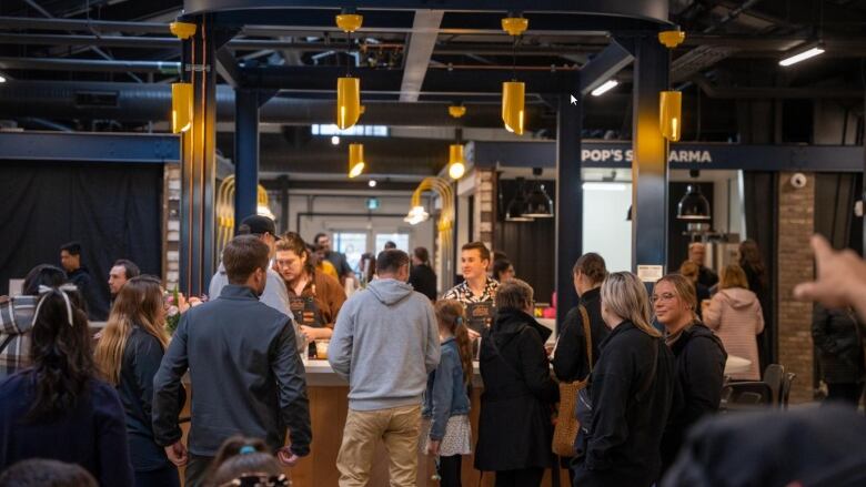 A bar with people getting drinks sits in the middle of a busy market.