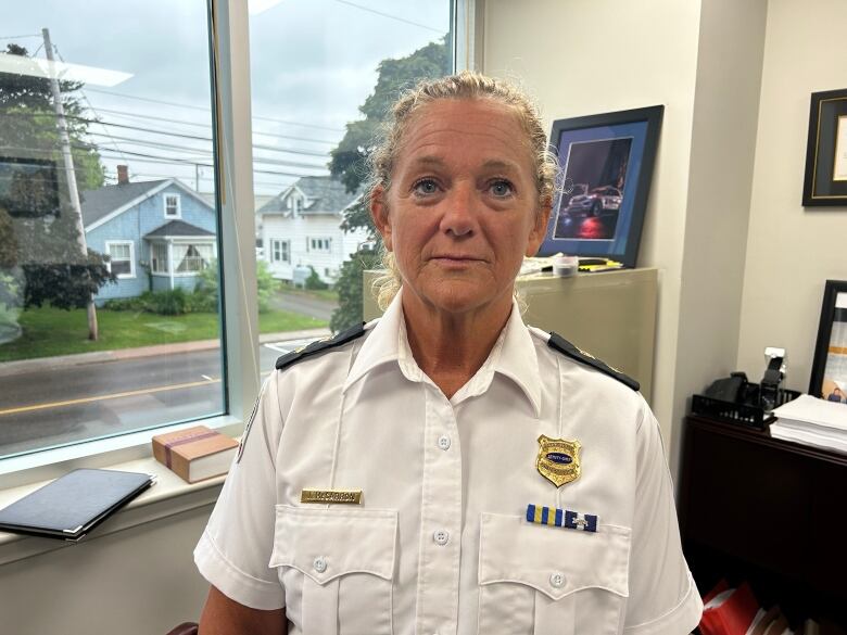 A woman with long light-coloured hair in a ponytail wearing a white police uniform standing in an office.