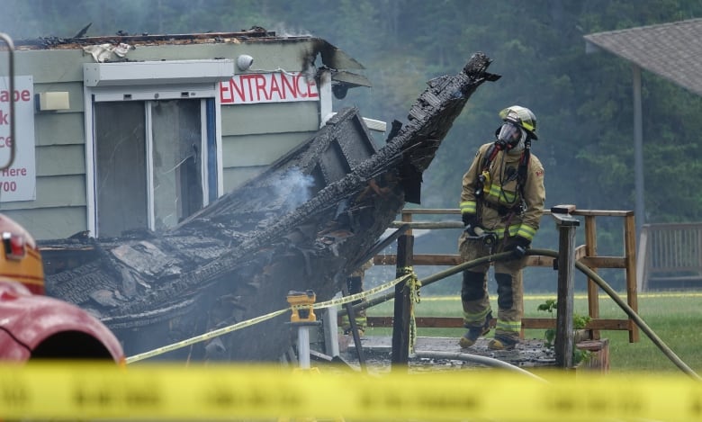 A firefighter is seen looking at a charred building. In the foreground is yellow police tape.