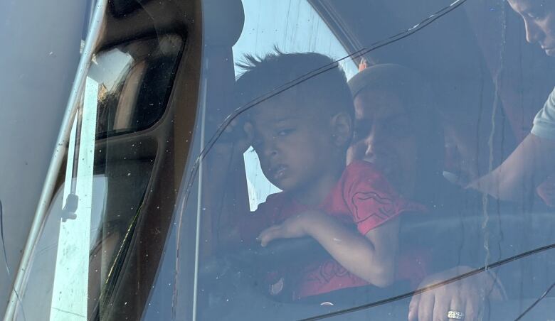 A young boy in a red T-shirt sits on his grandmother's lap inside a passenger bus.