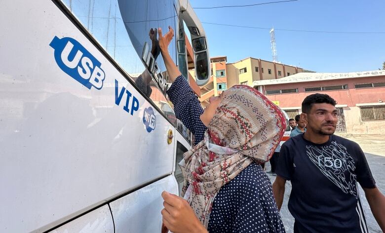 A young mother reaches her hand to touch the window of the passenger bus her five-year-old son is sitting inside.