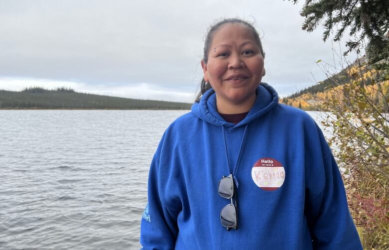 A woman in a blue hoodie stands beside a lake.