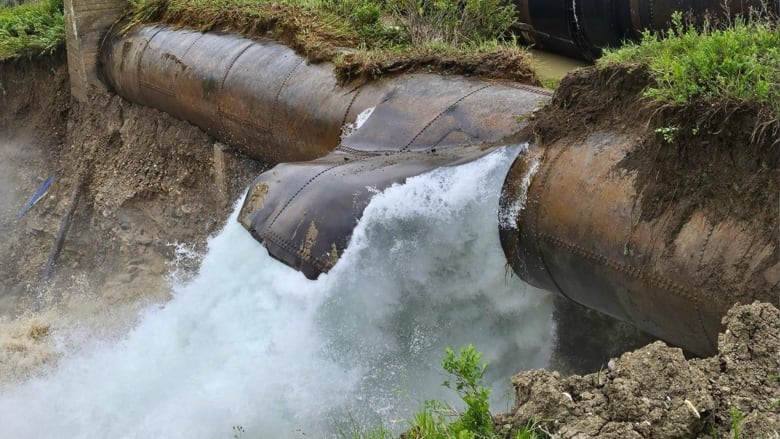 Water is bursting from a pipe and onto dirt.