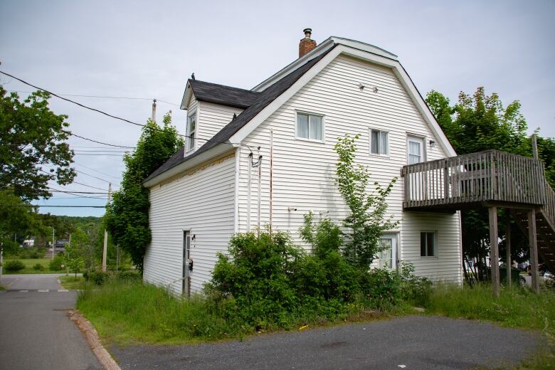 A two-storey white century home is pictured next to an overgrown lawn on a quiet street.