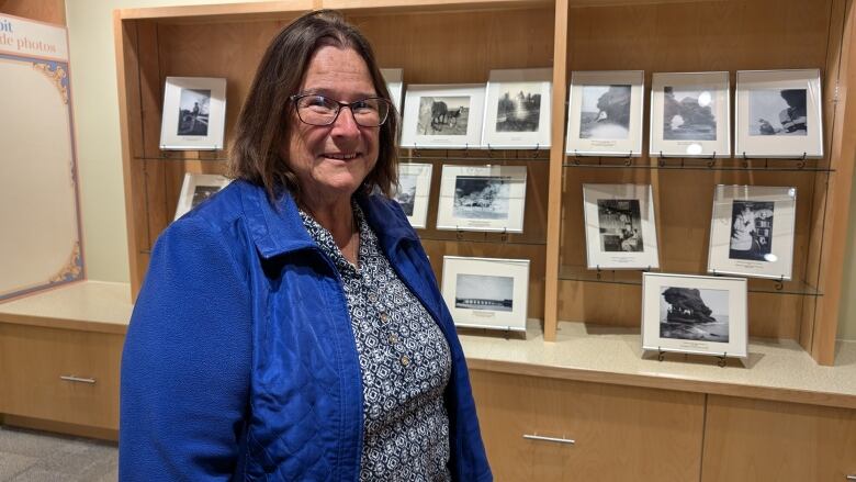 A woman in a blue jacket stands in front of an exhibit of black and white photos. 