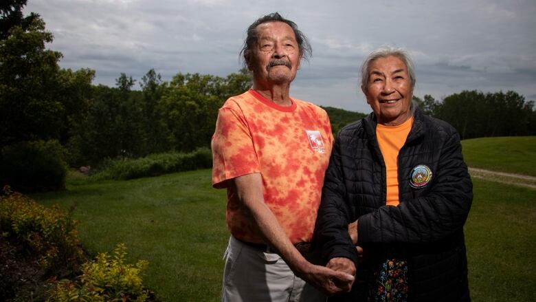 An elderly couple stands holding hands.