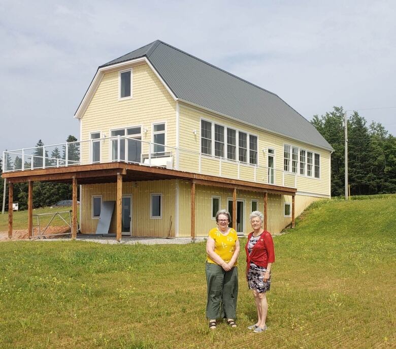 Two women stand in front of a yellow building.