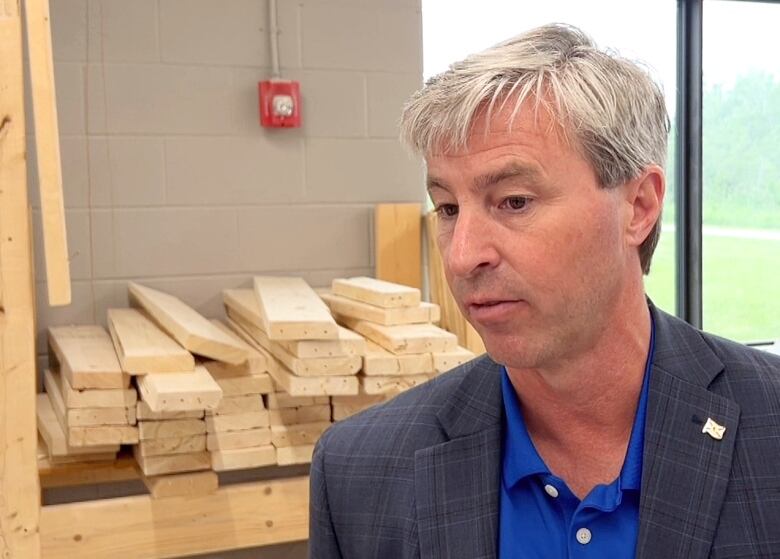 Tim Houston is seen in a workshop with a window and planks of wood behind him.