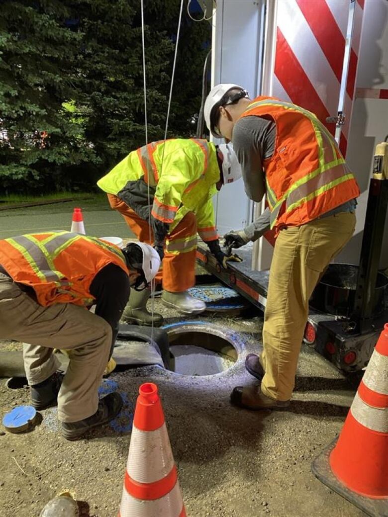 Men in safety vests hunch over around a large hole in the ground. 