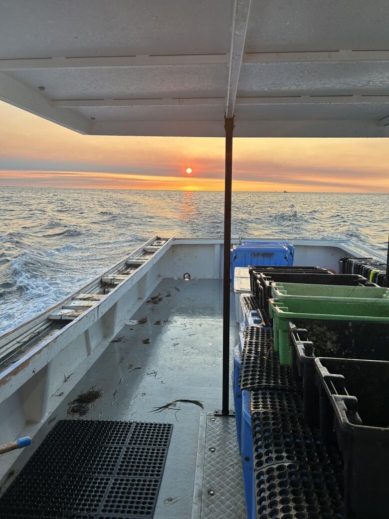 The back of a lobster boat with a rising sun visible in the background. 