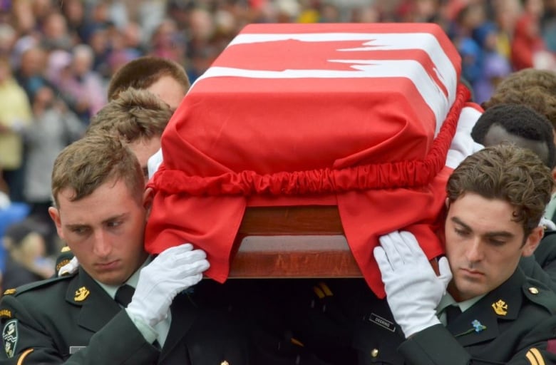 Solider carrying a casket draped in a Canadian flag. 