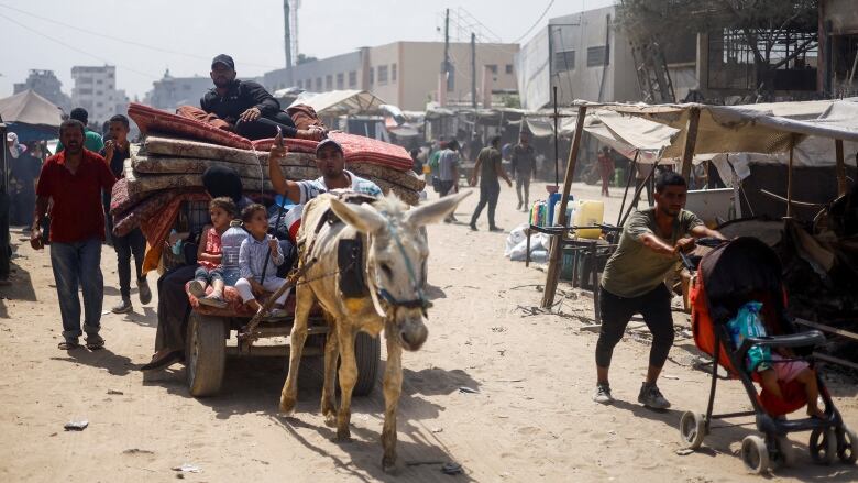 People ride on an animal-drawn cart loaded with belongings.