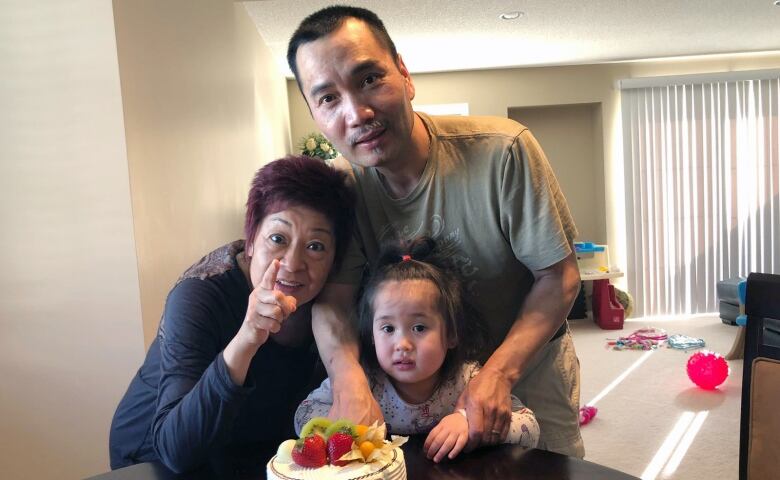 A man, a woman and a young girl with a birthday cake.