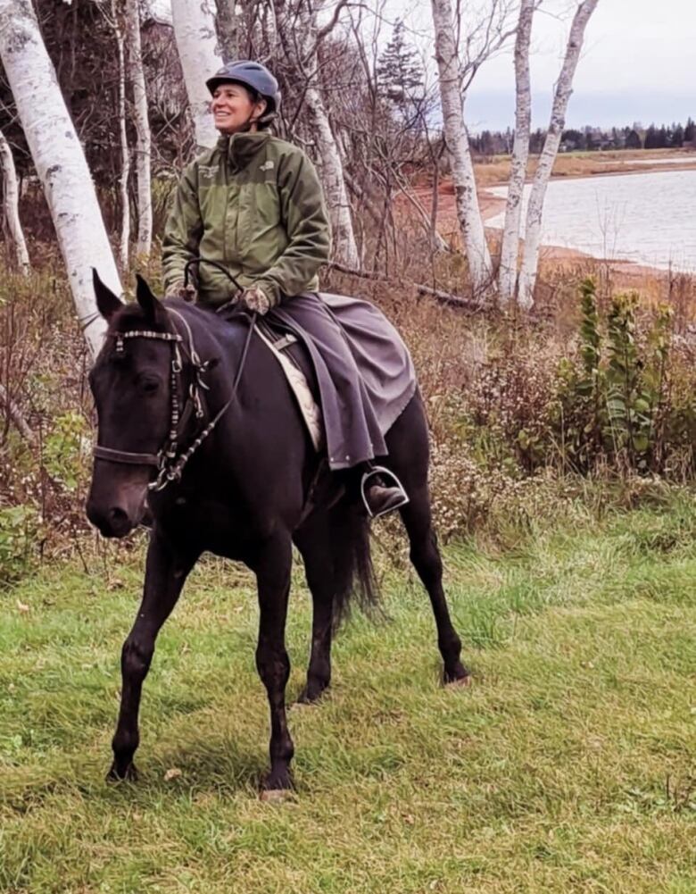 A woman in a riding helmet and dark green jacket sits atop a dark brown horse.