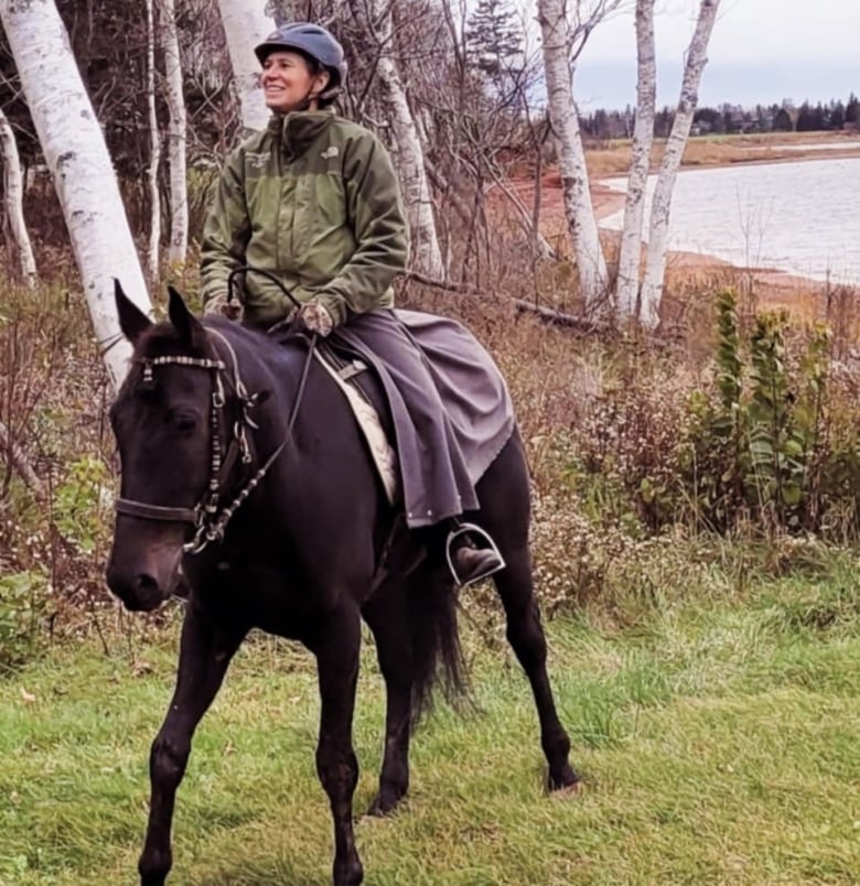 A woman in a riding helmet and dark green jacket sits atop a dark brown horse.