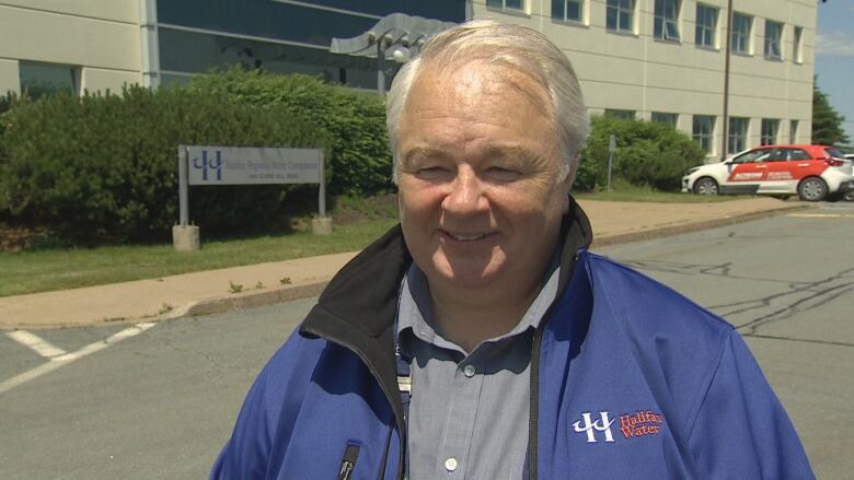 Man in blue jacket stands in front of building.