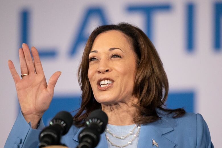 A woman smiles and gestures while speaking into a microphone.