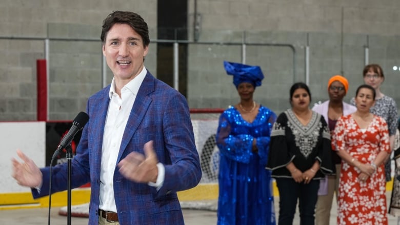 Trudeau stands in front of a microphone in a Montreal ice arena wearing a blue blazer and taking questions from reporters. 