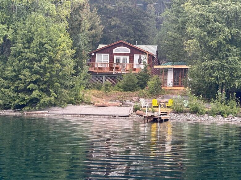 A cabin stands in a wooded area on a lake with a dock and jutting out into the water.