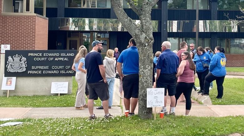 People crowd around the entrance to a large brick court building. 