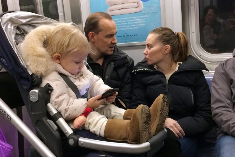 A baby girl plays with a mobile phone while riding in a New York subway.