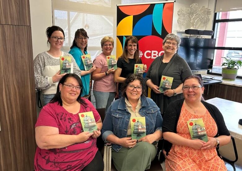 Book club members smile at the camera holding a book.