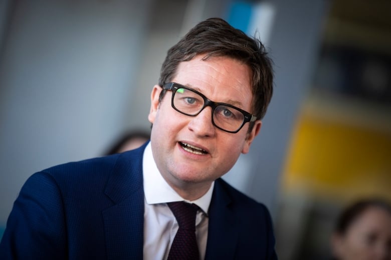 An image of a man wearing glasses at a news conference. 