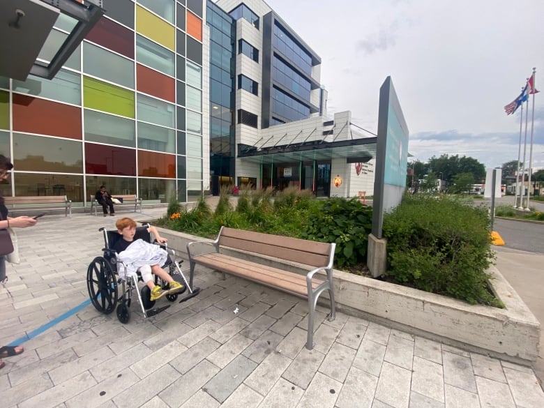 boy sits in wheelchair outside hospital