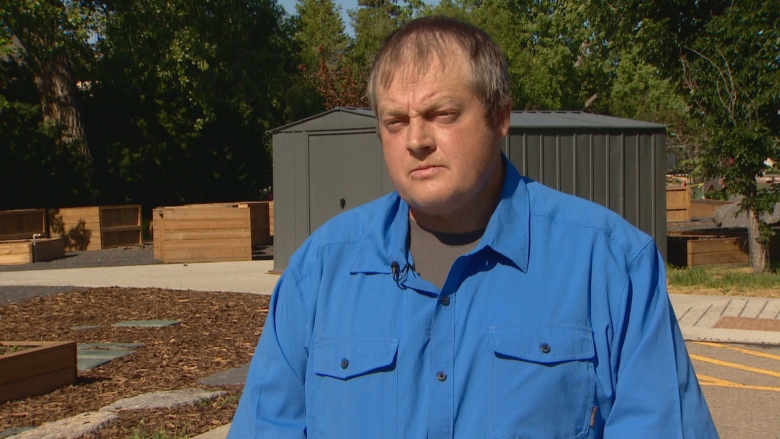 A man in a blue shirt stands in front of a row of raised garden beds.