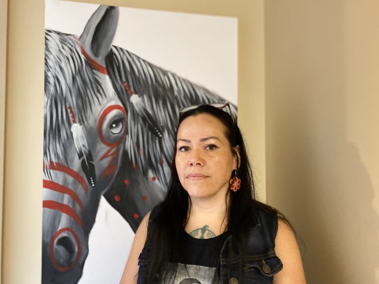 A women with her hair down stands in front of a horse portrait.