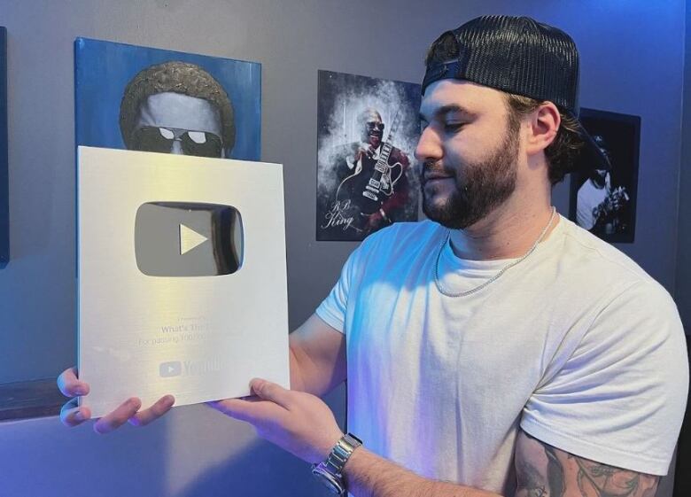 A man poses with an award in the shape of the YouTube logo, which is a rectangle with a triangle in the center of it. 