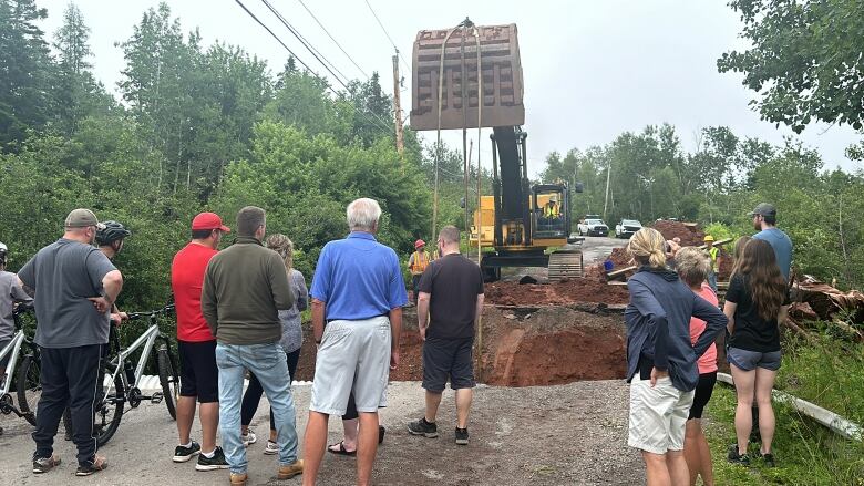 Multiple people watching repairs being done on a road 