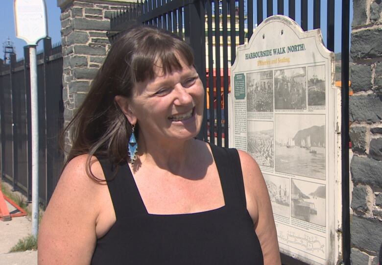 A woman stands in front of a metal fence with stone pillars. 