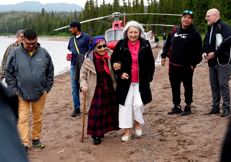 A group of people walk away from a helicopter with trees and mountains behind them. 