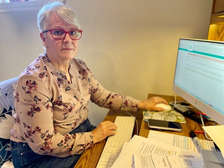 Paula Biggar sits at her computer desk with several papers piled on it. 