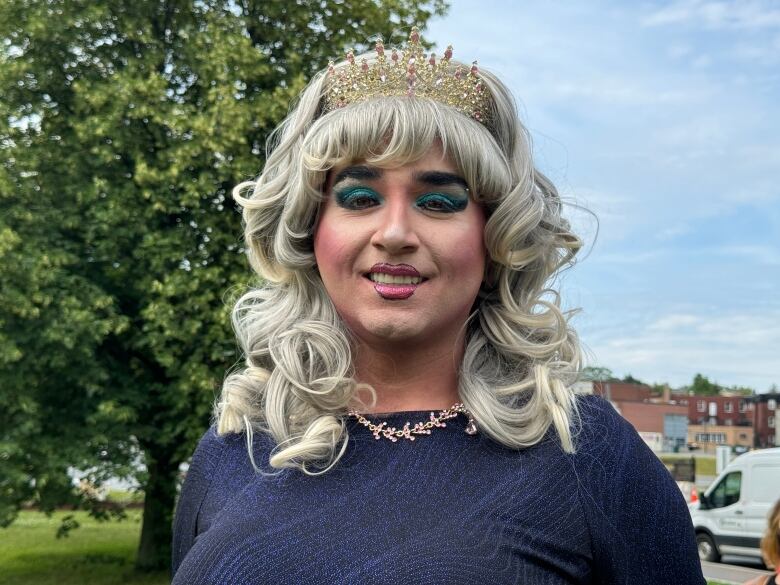 A person with blonde, curly hair and a crown smiles at the camera