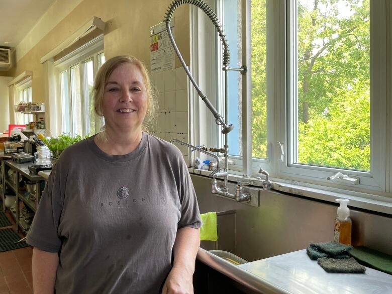 Jody Henderson, in a grey t-shirt, leans against the sink in a industrial kitchen. 