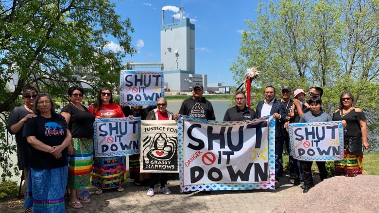 People are seen standing outside of an industrial plant carrying signs. 