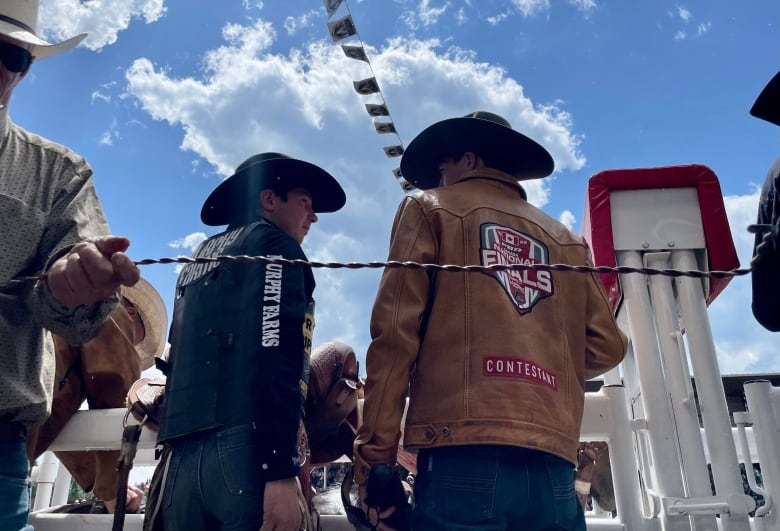 Two cowboys talk to eachother beside the bucking chutes.