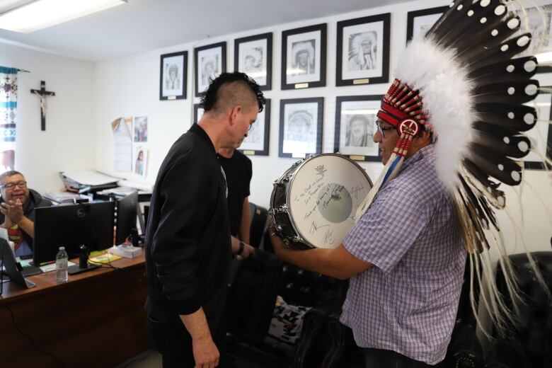 A punky band presents a chief wearing a headdress with a signed drum. 