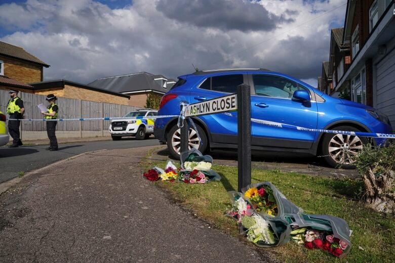 Bouquets of flowers lay on the grass at the bottom of a sign that reads 